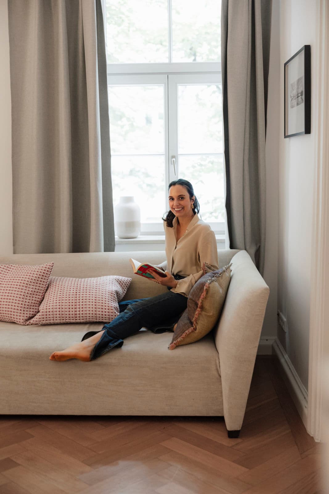 Eine Frau sitzt lächelnd mit einem Buch auf dem Sofa